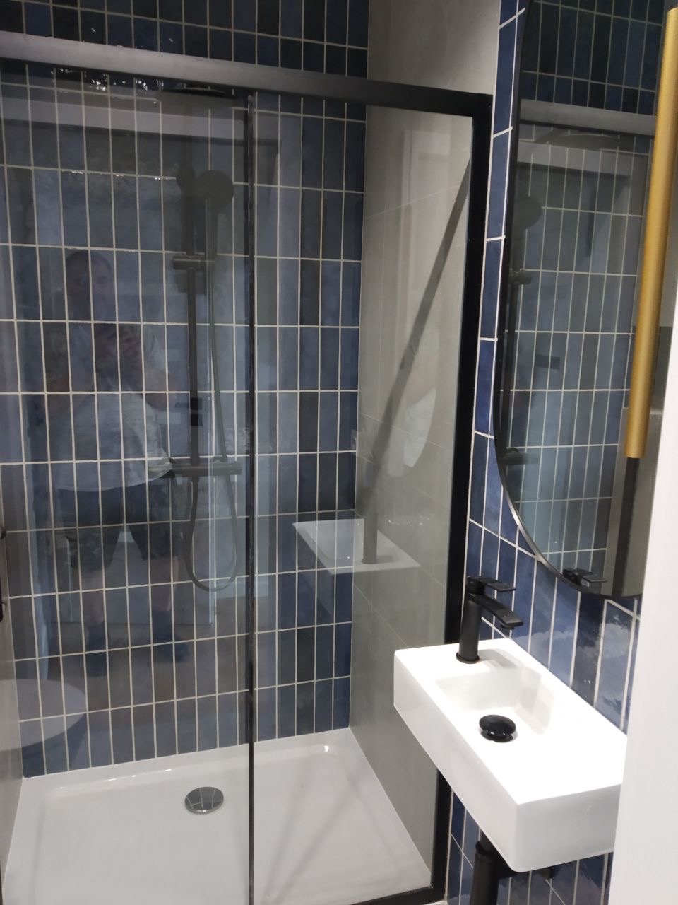 Nowoczesna łazienka z kabiną prysznicową w czarnej ramie, umywalką nablatową i niebieskimi płytkami ułożonymi pionowo.