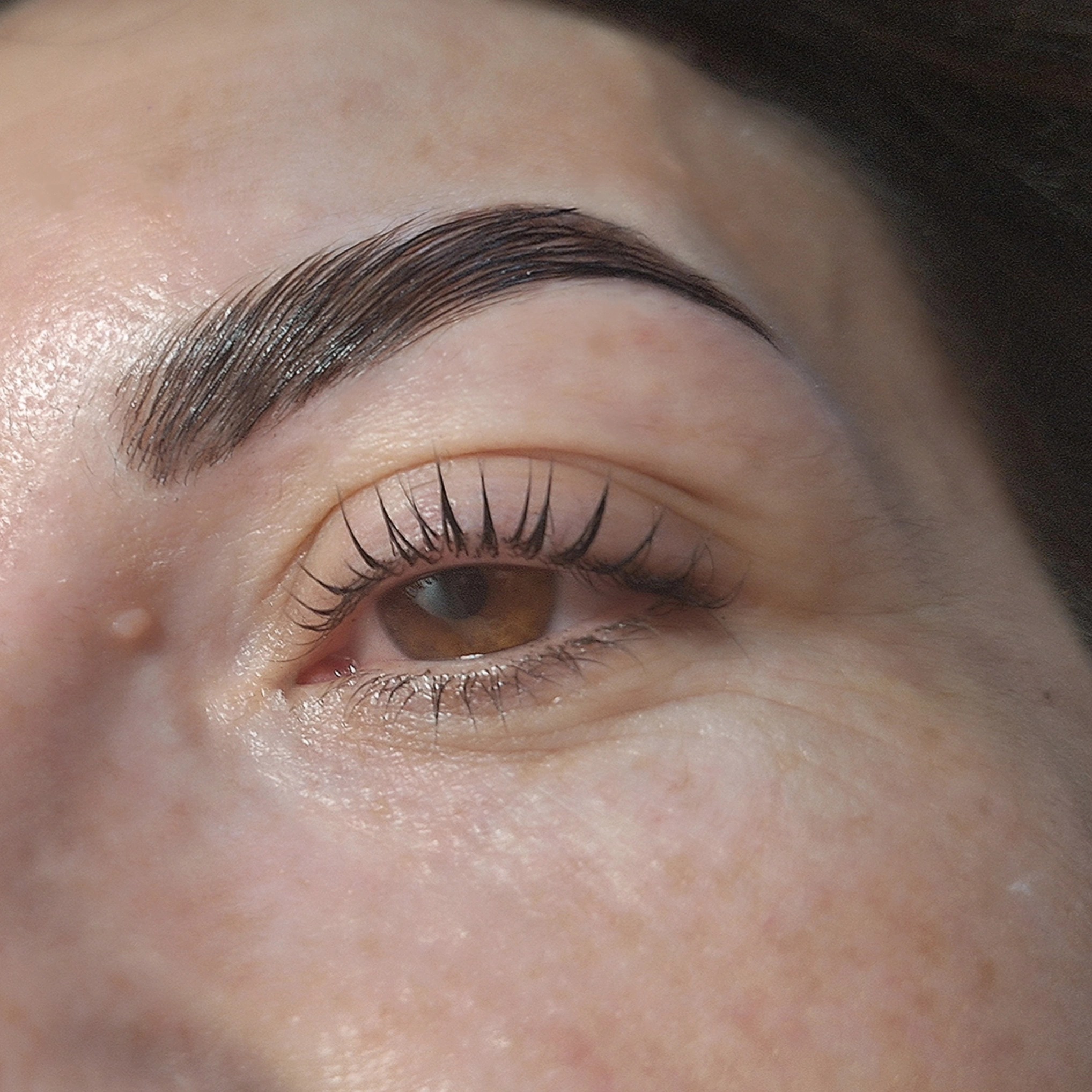 Zbliżenie na oko z widocznymi, świeżo wystylizowanymi brwiami i rzęsami. Widoczny efekt laminacji brwi i liftingu rzęs. Jasna karnacja.