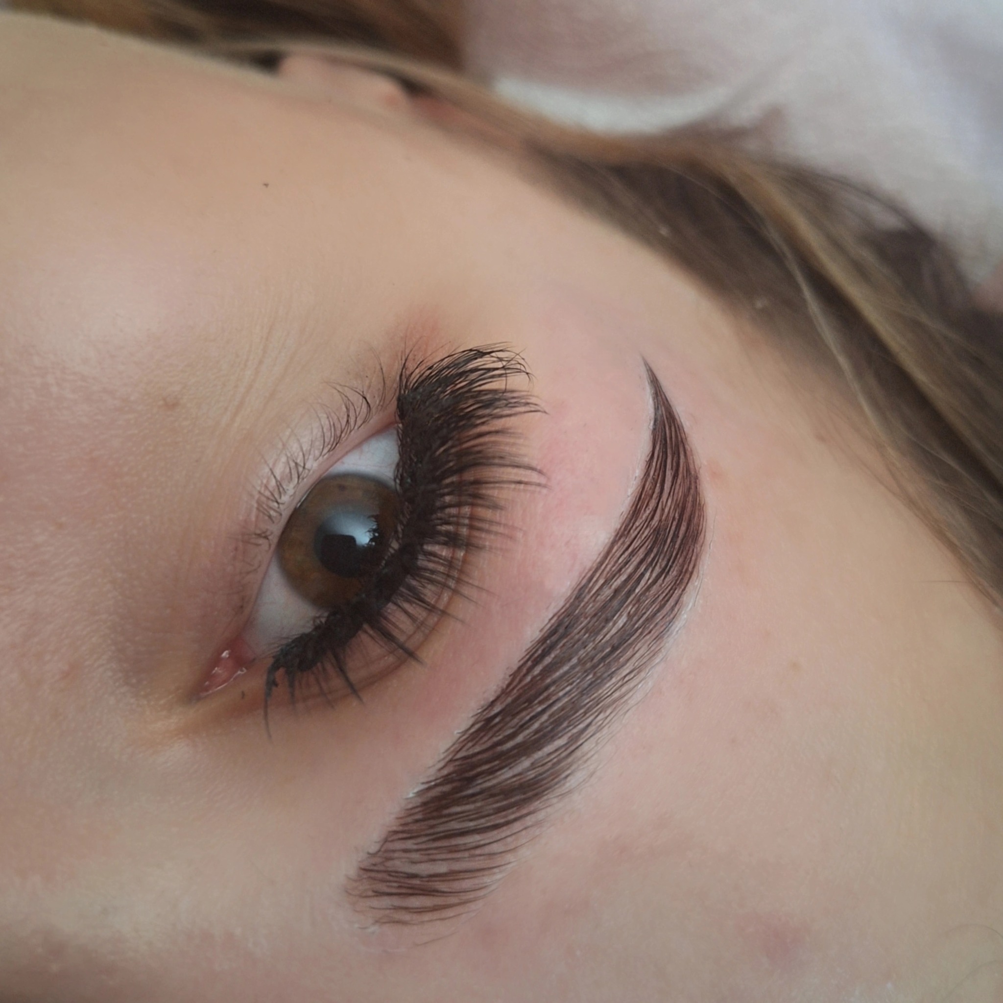 Zbliżenie na oko z długimi rzęsami i wystylizowaną brwią. Widoczne pojedyncze włoski. Delikatny makijaż podkreśla naturalne piękno.