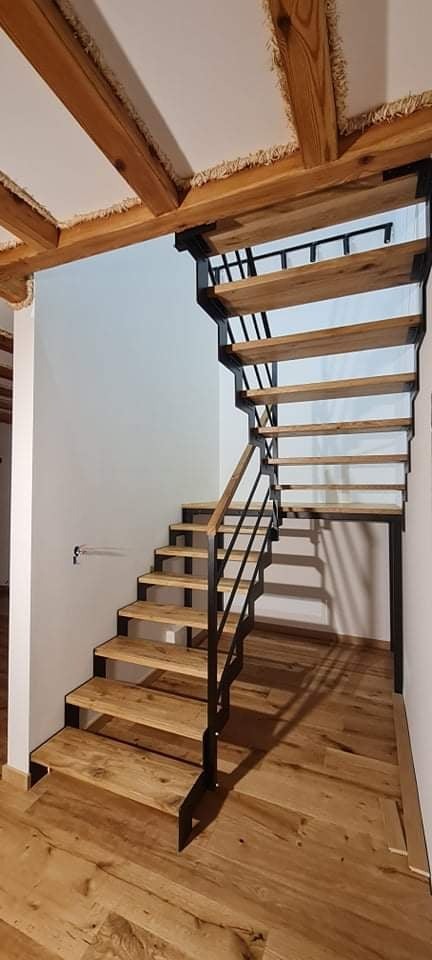 Drewniane schody z czarną, metalową konstrukcją w surowym wnętrzu z drewnianym stropem i podłogą z desek.