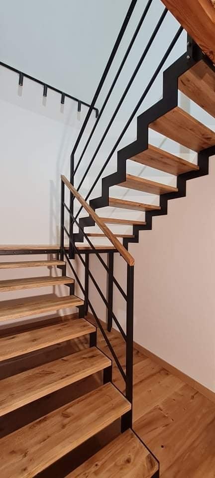 Nowoczesne schody z drewnianymi stopniami i czarną metalową konstrukcją, oświetlenie punktowe na suficie, widok z dołu.