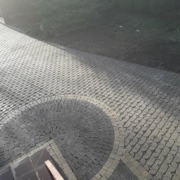 Łukasza Wojtak - Ułożona kostka granitowa w kształcie wachlarza przy schodach, obrzeża z jaśniejszej kostki, dalsza część ścieżki z kostki o ażurowym wzorze wypełnionym drobnym kamieniem.