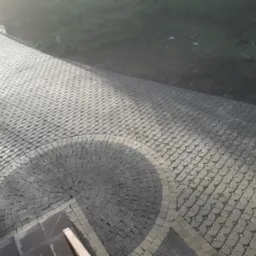 Ułożona kostka granitowa w kształcie wachlarza przy schodach, obrzeża z jaśniejszej kostki, dalsza część ścieżki z kostki o ażurowym wzorze wypełnionym drobnym kamieniem.