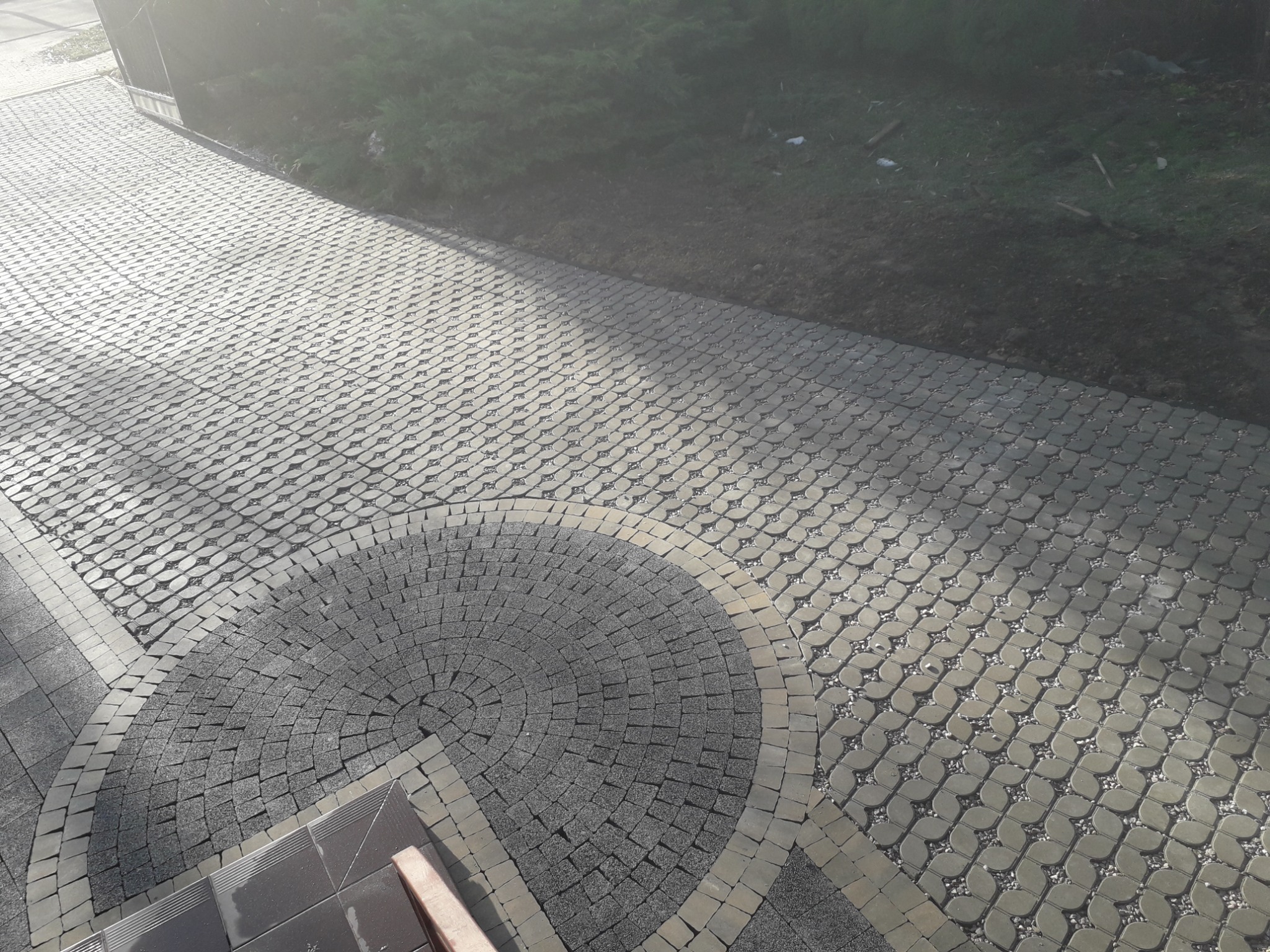 Ułożona kostka granitowa w kształcie wachlarza przy schodach, obrzeża z jaśniejszej kostki, dalsza część ścieżki z kostki o ażurowym wzorze wypełnionym drobnym kamieniem.