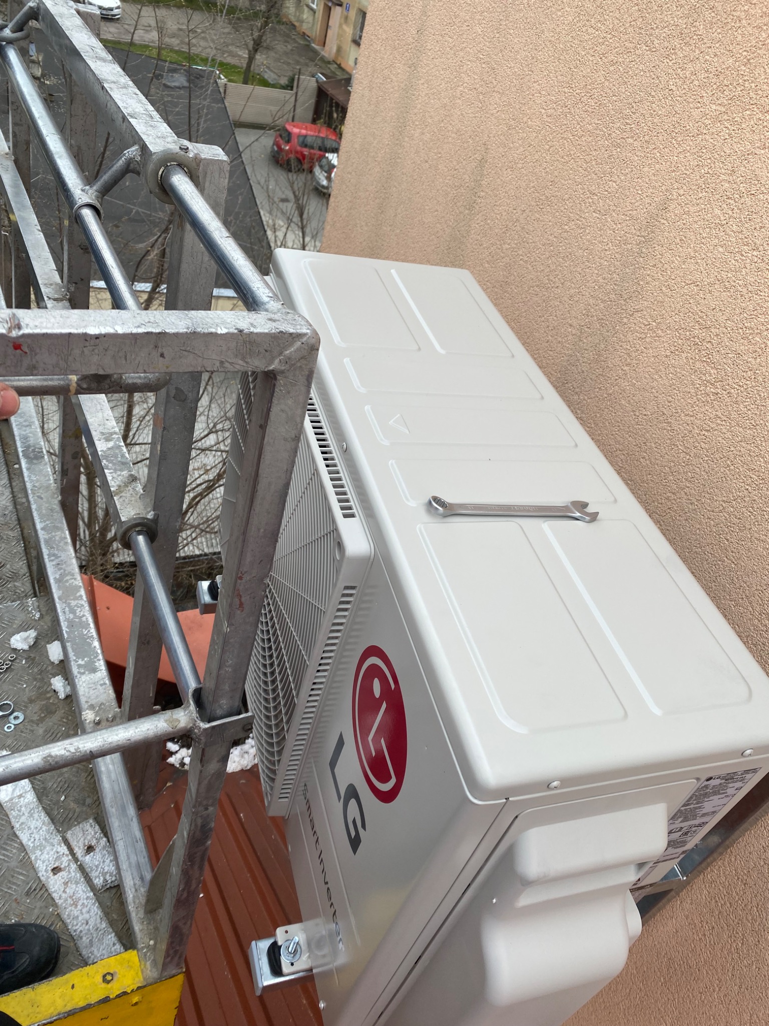 Montaż zewnętrznej jednostki klimatyzacji LG Smart Inverter z drabiny, klucz leży na obudowie, widok z góry.