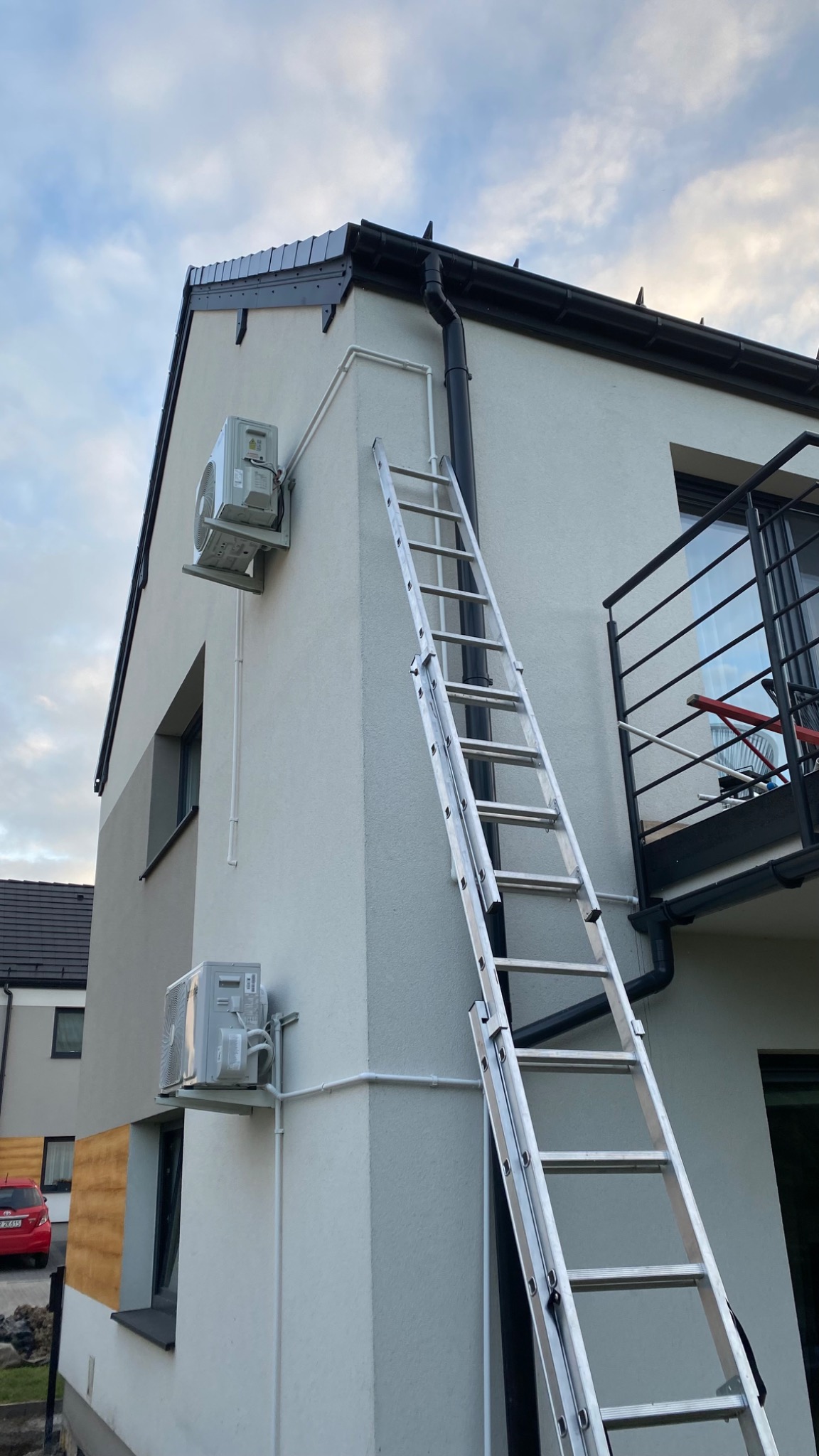Dwa klimatyzatory zamontowane na elewacji domu jednorodzinnego, drabina oparta o ścianę, widoczne rury odprowadzające skropliny.