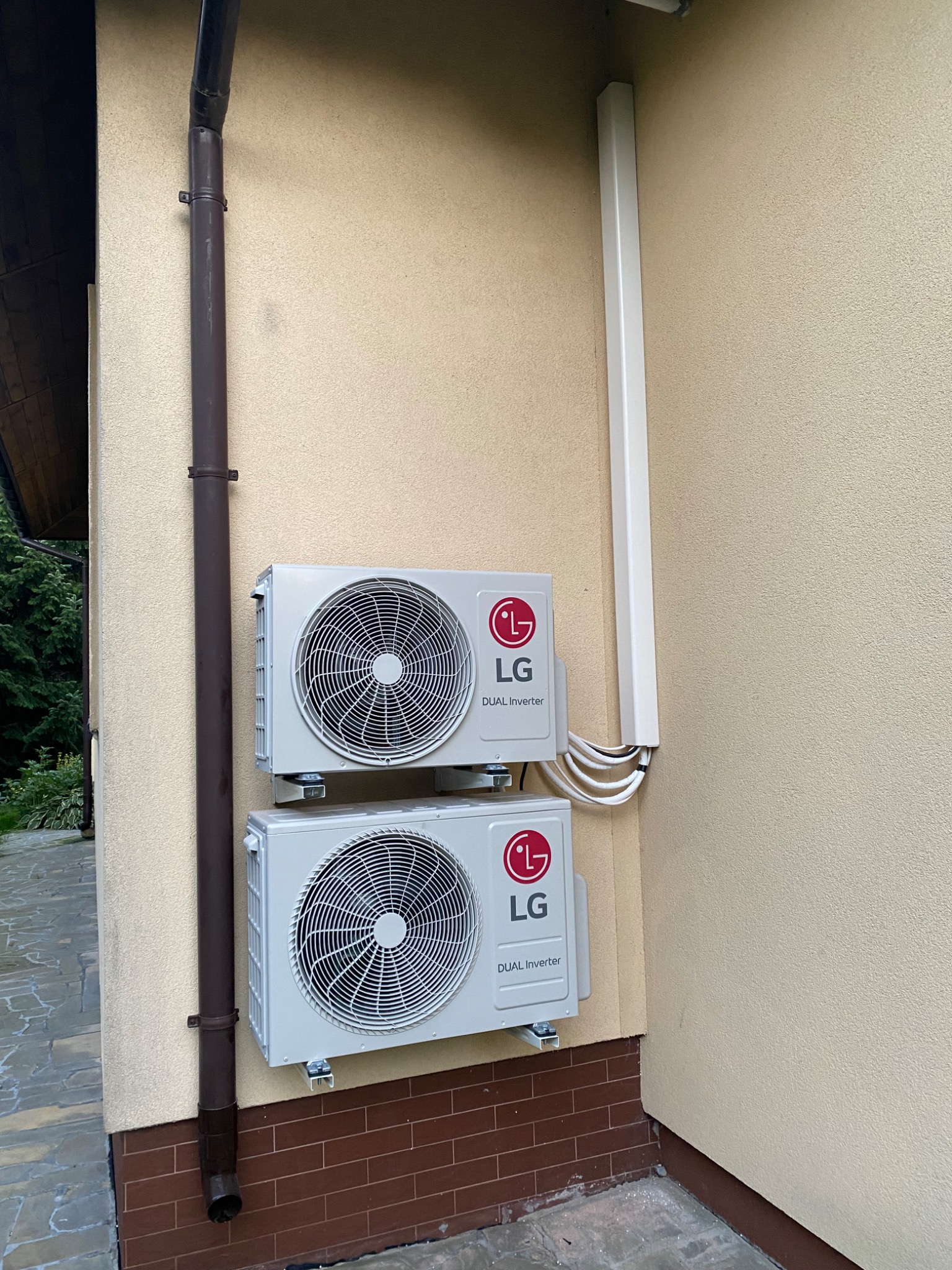 Dwa zewnętrzne moduły klimatyzacji LG Dual Inverter zamontowane na elewacji domu, z widoczną rurą spustową i osłoną przewodów.