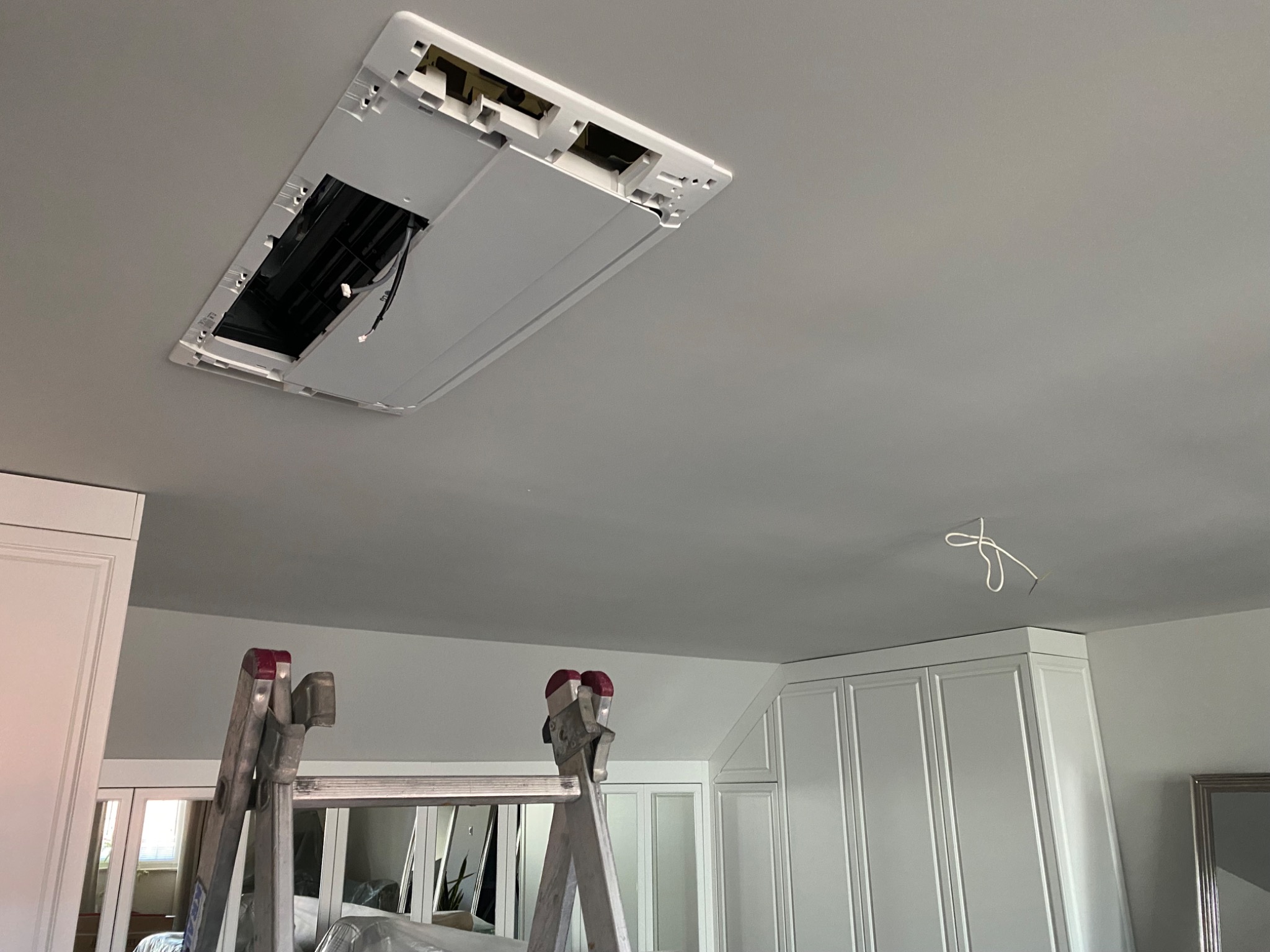 Montaż kasetonowej jednostki wewnętrznej klimatyzacji w Wieliczce, widok z drabiny, widoczne przewody i fragment zabudowy meblowej.