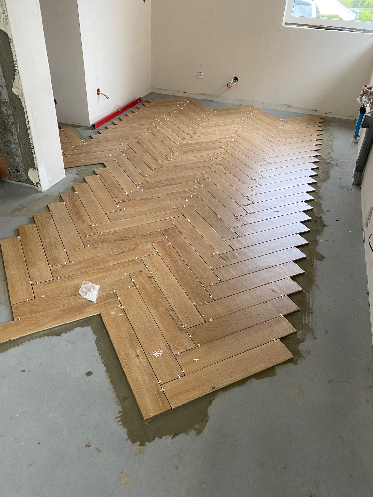 Układanie drewnopodobnych płytek podłogowych w jodełkę, z użyciem białych krzyżyków dystansowych, na wylewce podłogowej w trakcie remontu.