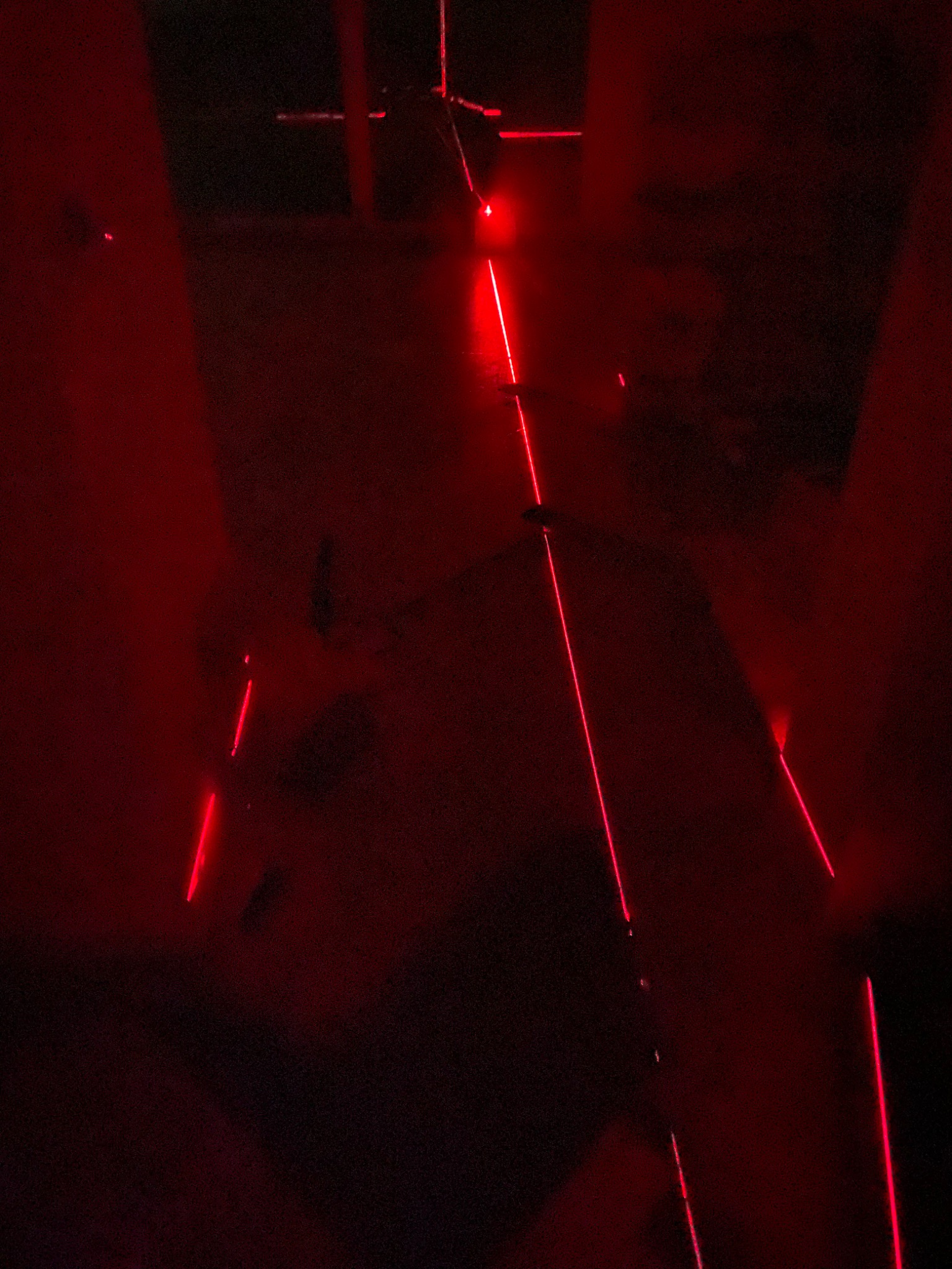 Czerwone wiązki lasera w ciemnym pomieszczeniu, prawdopodobnie podczas instalacji lub testowania systemu klimatyzacji.