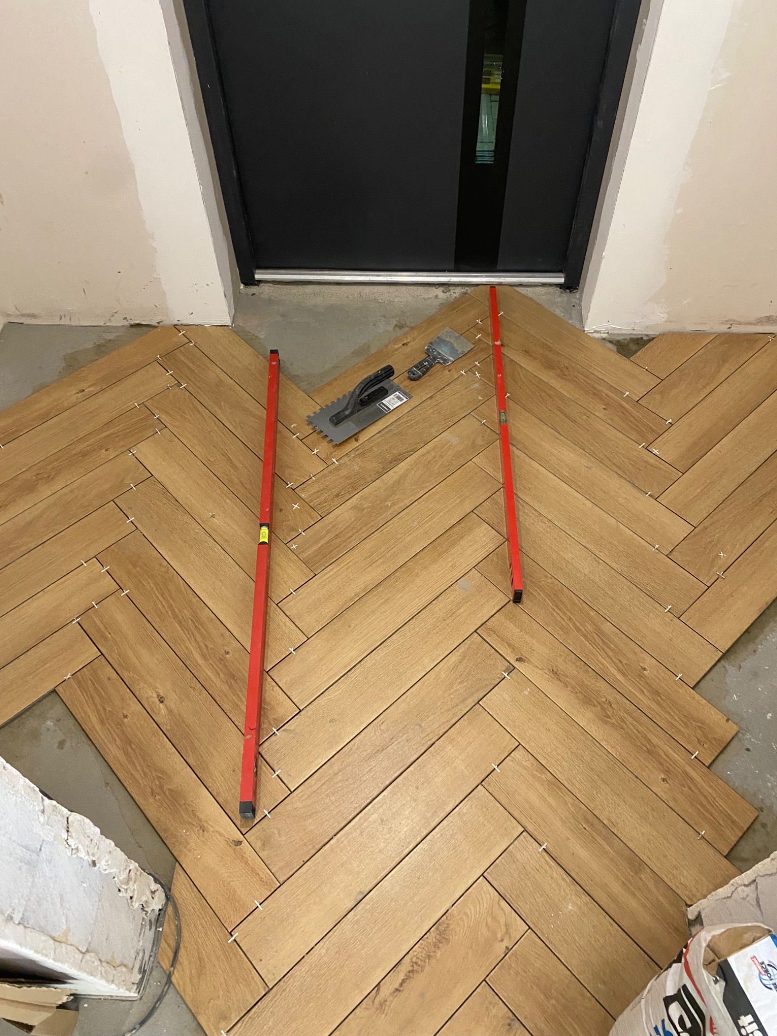 Układanie parkietu w jodełkę w przedpokoju, widoczne poziomice, szpachelka i krzyżyki dystansowe.