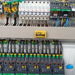 Rozdzielnica elektryczna z widocznymi bezpiecznikami, stycznikami Schneider Electric TeSys, okablowaniem oznaczonym żółtymi etykietami i zabezpieczeniem antykorozyjnym Zerust Vapor Capsule.