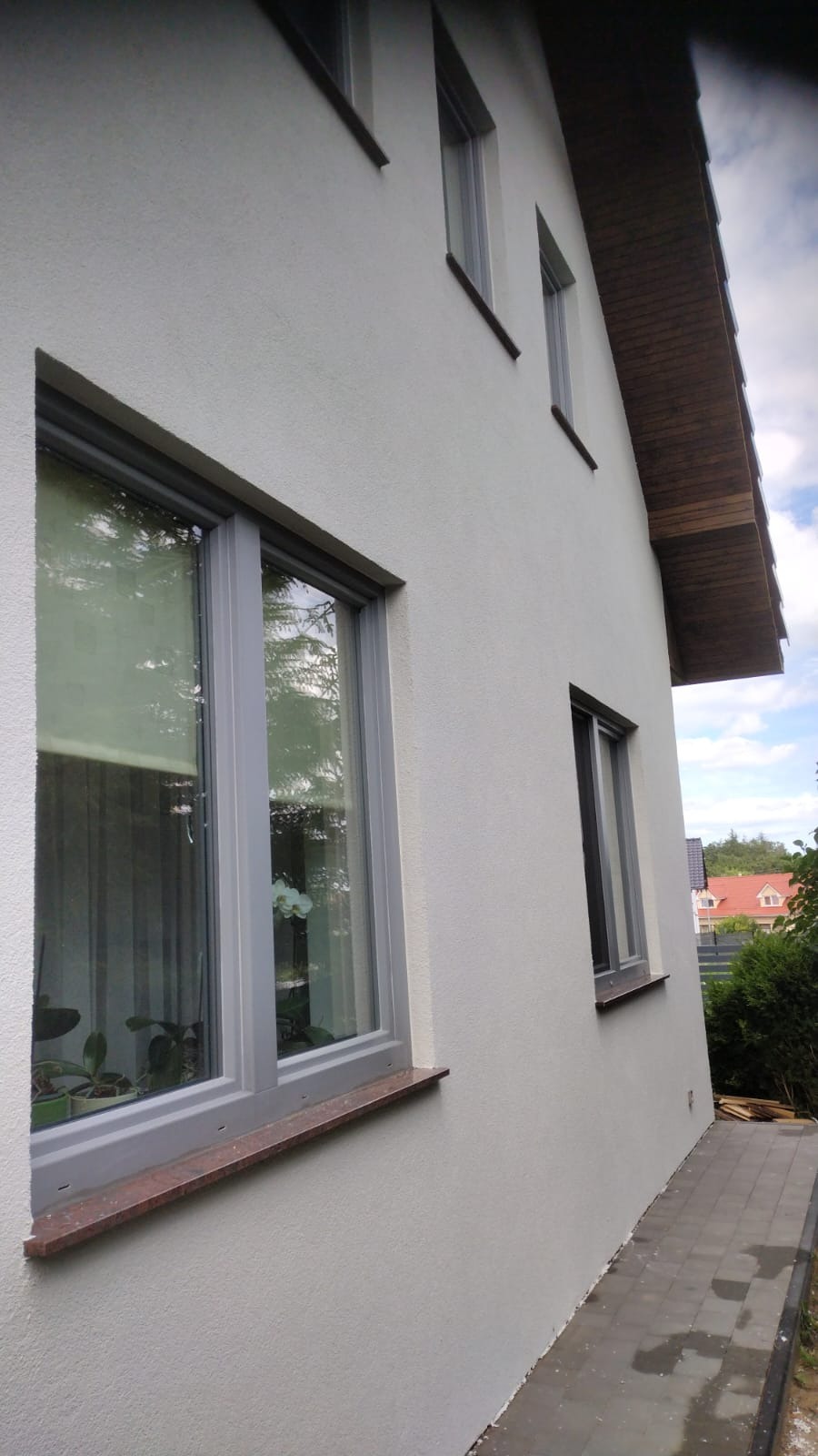 Świeżo otynkowana elewacja budynku mieszkalnego w Starogardzie Gdańskim, widok z boku, szare ramy okienne, parapety z czerwonego granitu, obok ułożona kostka brukowa.