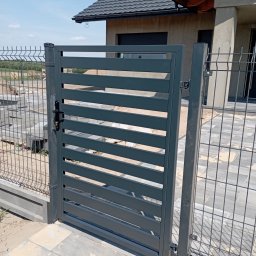 OLI LOOK Usługi Ślusarskie Hubert Podlesiński - Nowoczesna, antracytowa brama wjazdowa z poziomymi lamelami, z czarną klamką, dopasowana do ogrodzenia panelowego na tle domu z szarą dachówką.