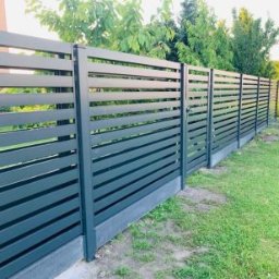 OLI LOOK Usługi Ślusarskie Hubert Podlesiński - Nowoczesne, poziome ogrodzenie panelowe w kolorze grafitowym, osadzone na niskiej, betonowej podmurówce, otoczone zielonym trawnikiem i drzewami.