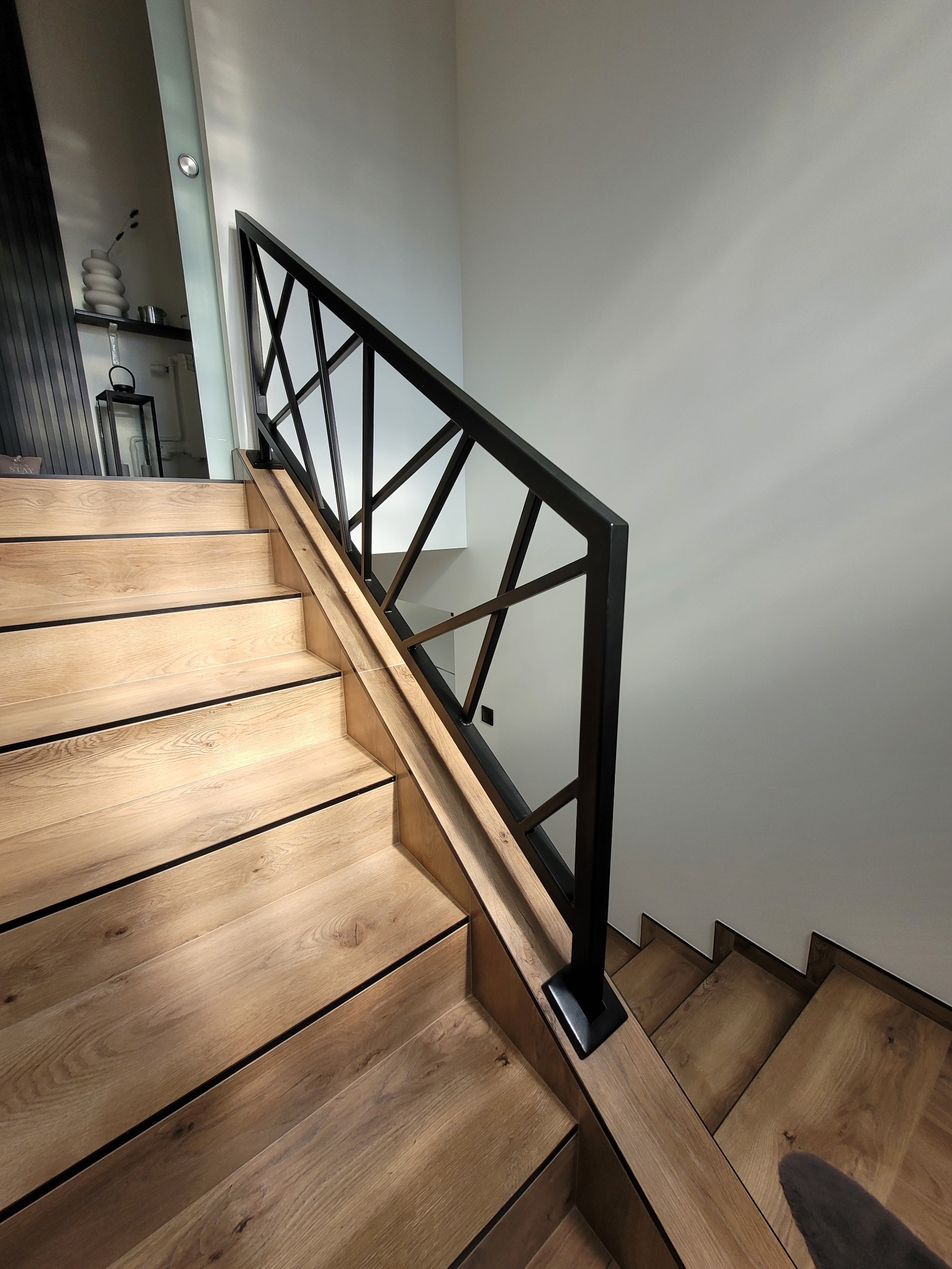 Schody drewniane z czarną, geometryczną balustradą metalową; widok z dołu, nowoczesny design.