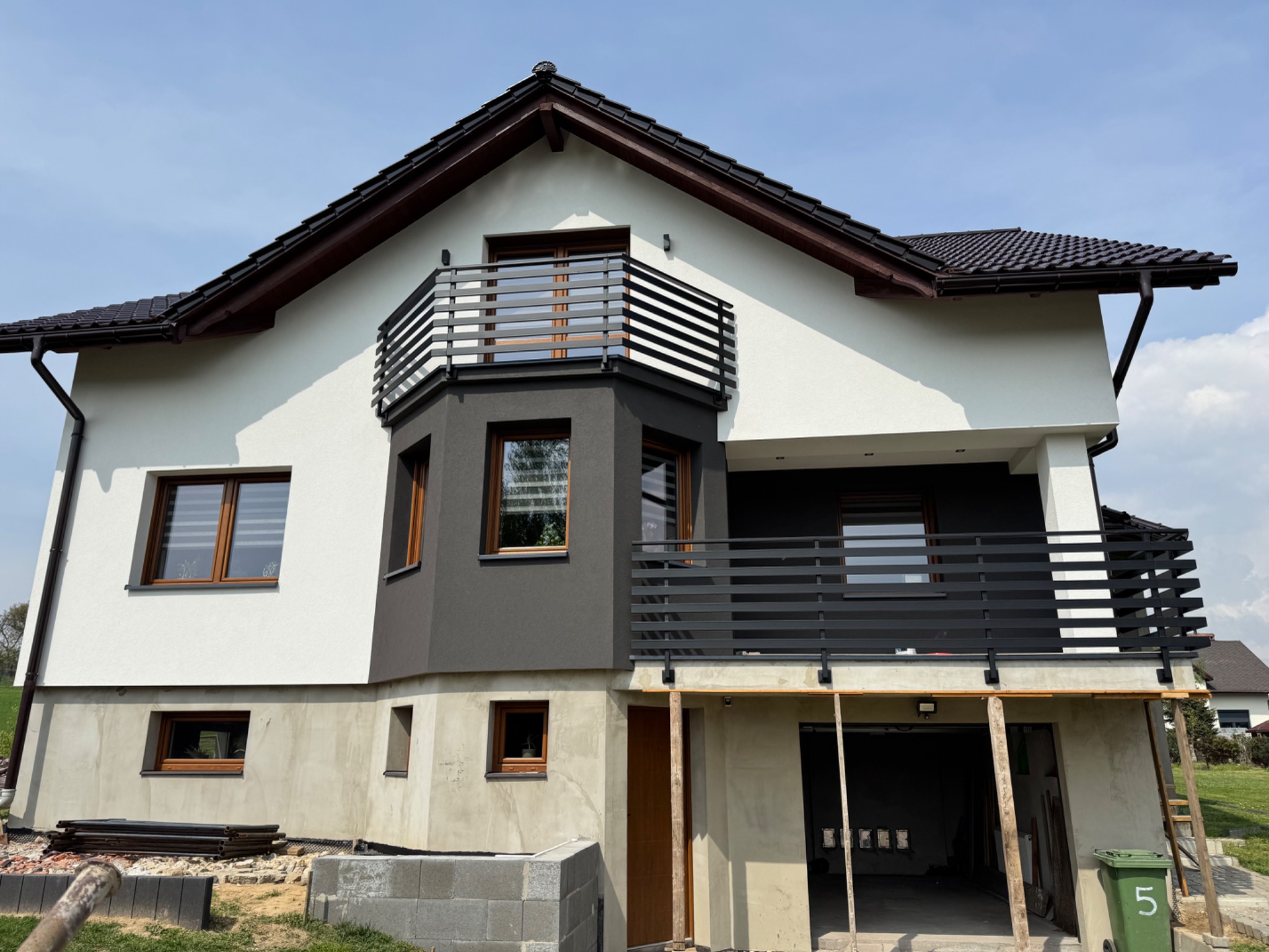 Nowoczesny dom z czarnymi, metalowymi balustradami balkonowymi w Czyżowicach. Widoczne detale wykończenia i surowy stan parteru.