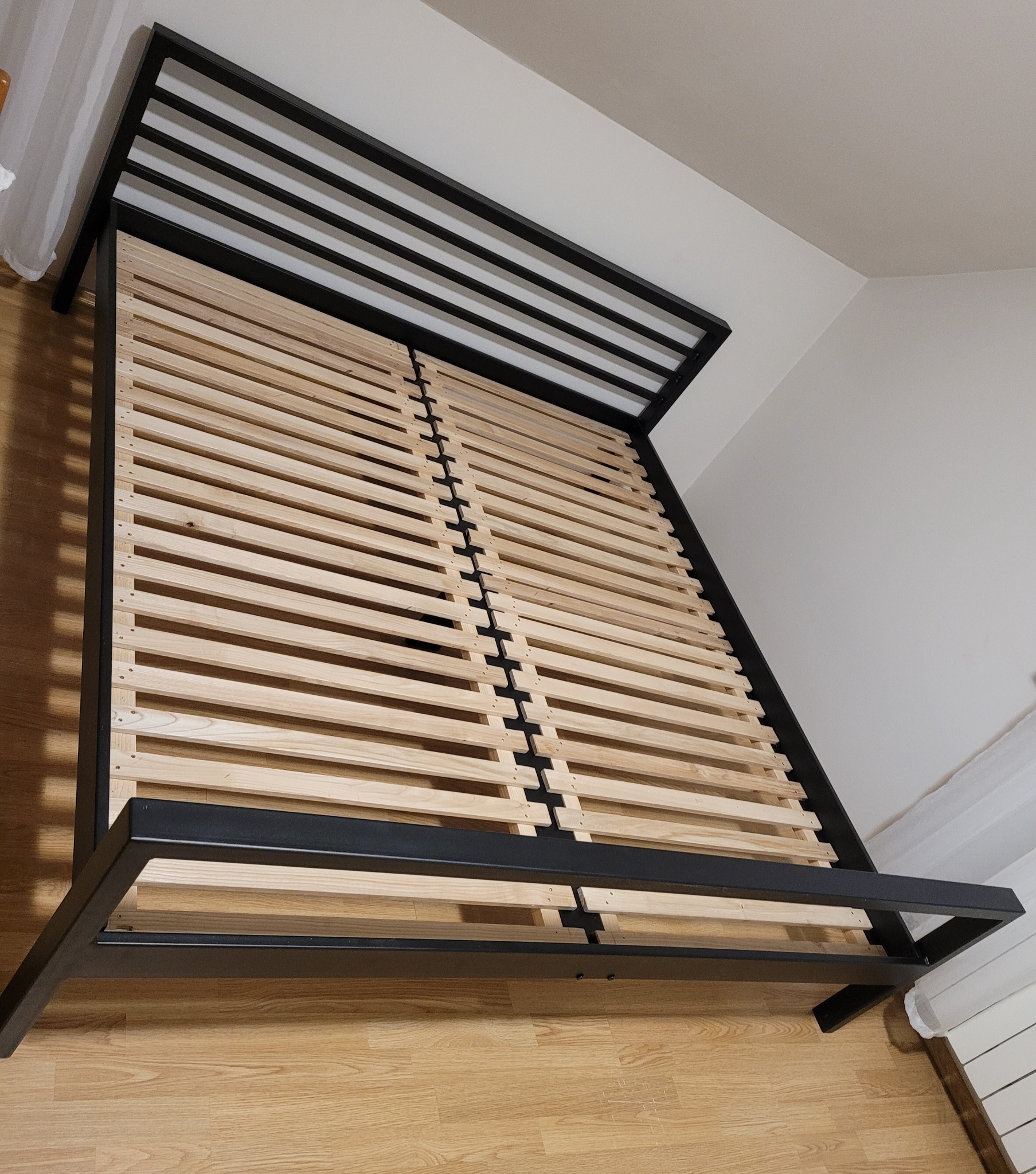 Metalowa rama łóżka z drewnianym stelażem, widok z góry pod kątem, na podłodze panele.