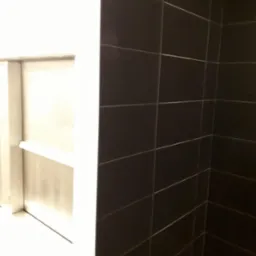Ciemne, prostokątne płytki ułożone na ścianie pod kątem, z widoczną wnęką z półką po lewej stronie.