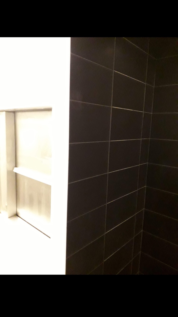 Ciemne, prostokątne płytki ułożone na ścianie pod kątem, z widoczną wnęką z półką po lewej stronie.