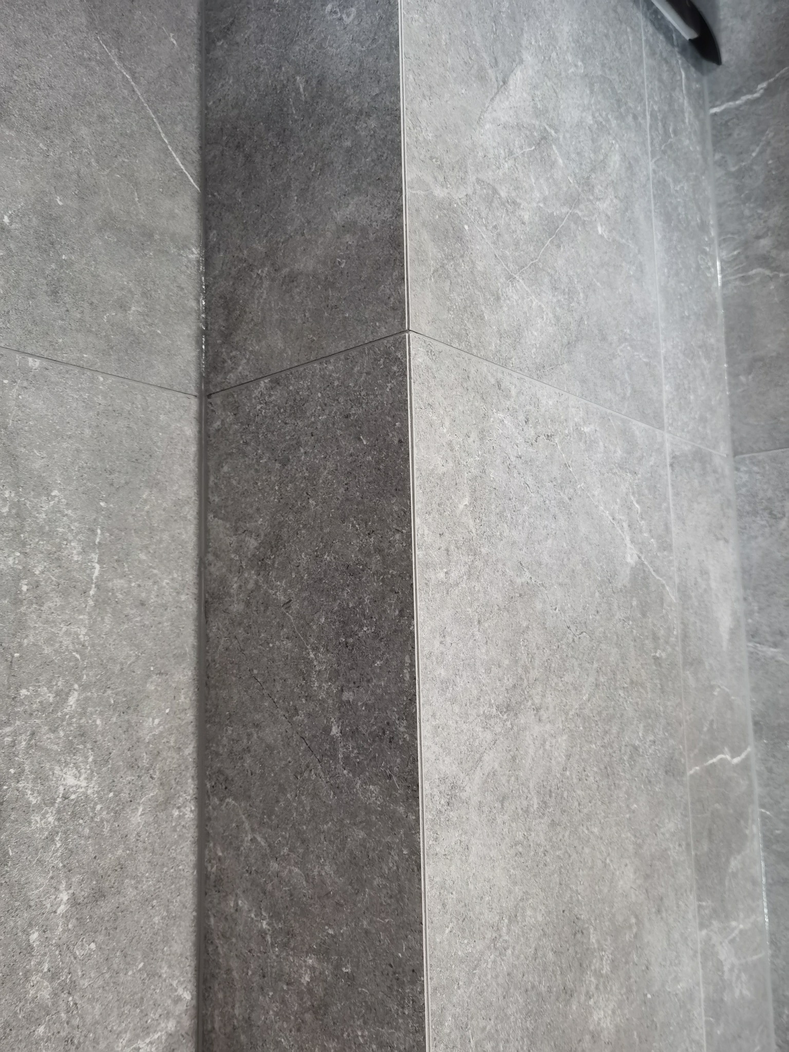 Szare płytki imitujące kamień, ułożone w rogu pomieszczenia, z widocznymi fugami.