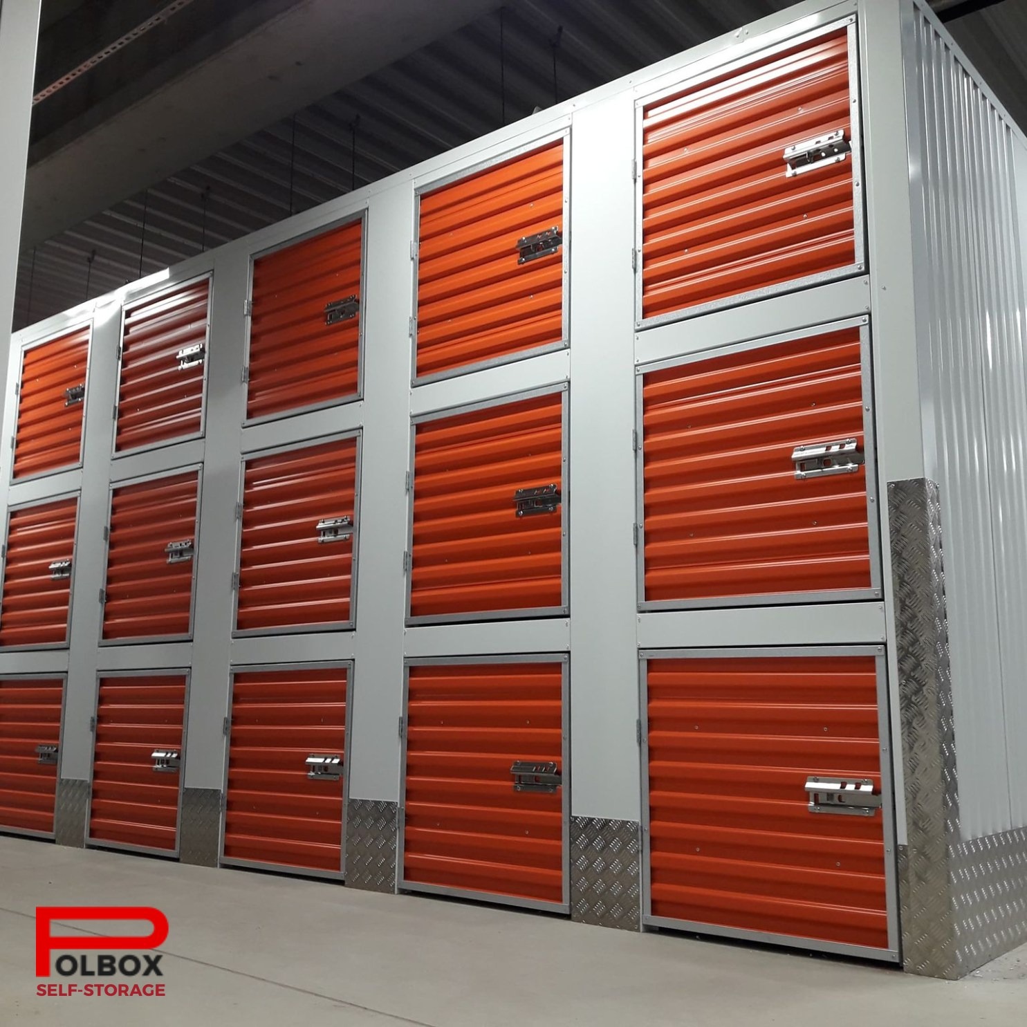 Rząd pomarańczowych, metalowych boksów do przechowywania, zabezpieczonych zamkami, z logo firmy na dole zdjęcia.