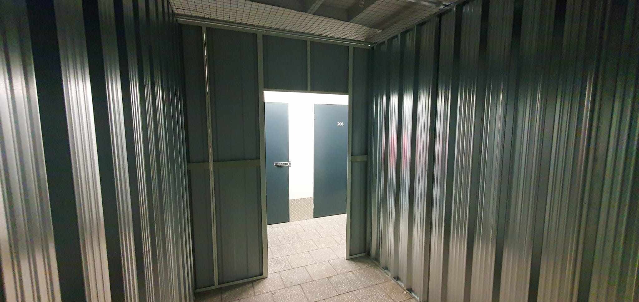 Wnętrze boksu z metalowymi ścianami i otwartymi drzwiami, widoczny numer 208 na drzwiach dalszego boksu.