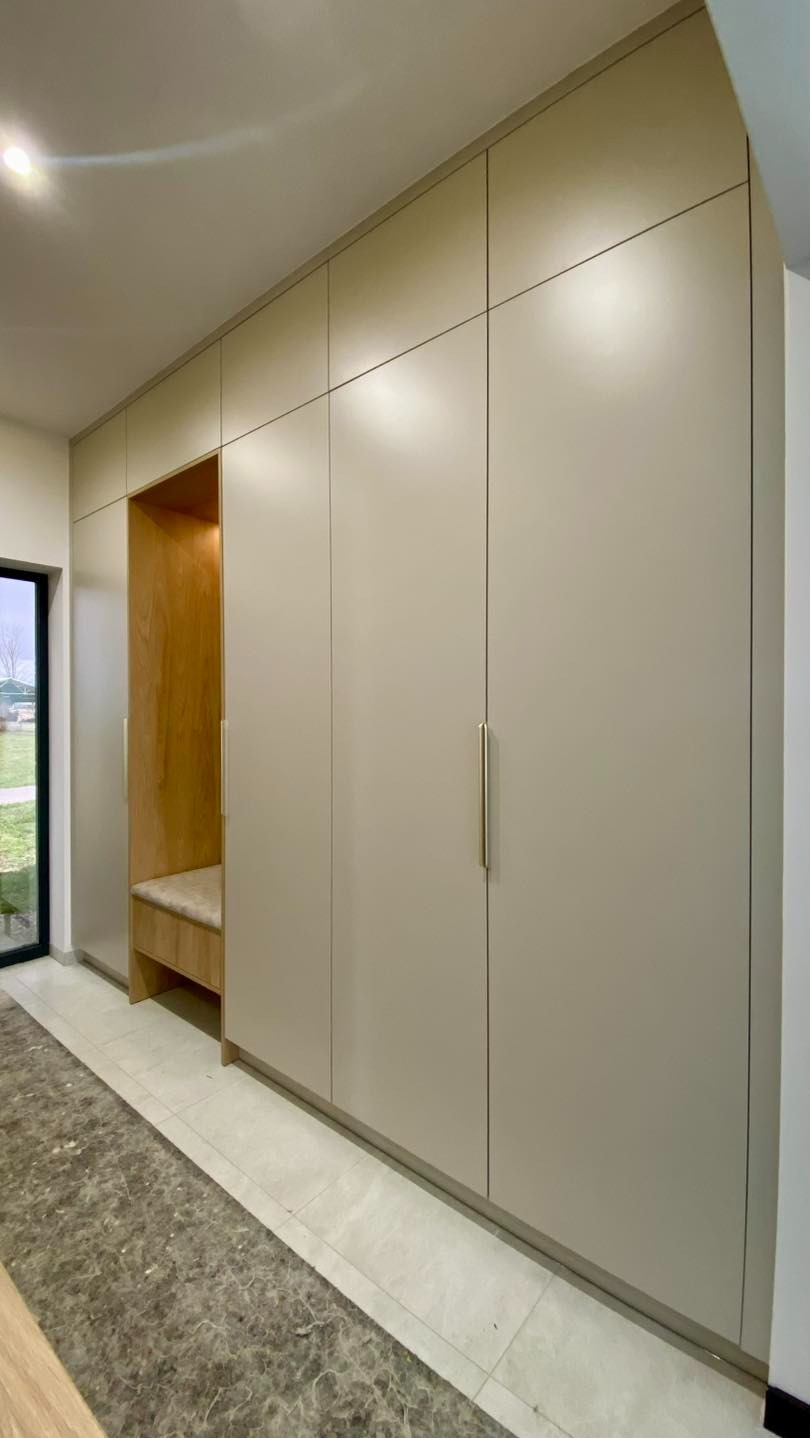 Beżowa szafa wnękowa z siedziskiem z jasnego drewna, minimalistyczny design, długie, złote uchwyty, widok z boku, nowoczesne wykończenie, płytki podłogowe.