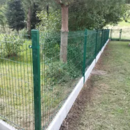 Nowoczesne, zielone ogrodzenie panelowe na betonowej podmurówce, widok z boku na tle zieleni ogrodowej i drzew.