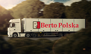 Biała ciężarówka z naczepą chłodnią z logo Berto Polska na tle rozmytego krajobrazu leśnego w słoneczny dzień.