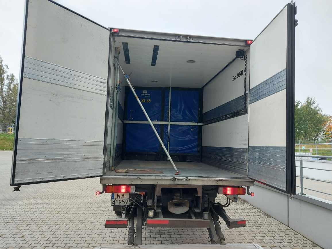 Otwarta przestrzeń ładunkowa samochodu dostawczego z zabezpieczonym ładunkiem w postaci niebieskich kontenerów, widoczne podpory zabezpieczające ładunek i tylne światła pojazdu.