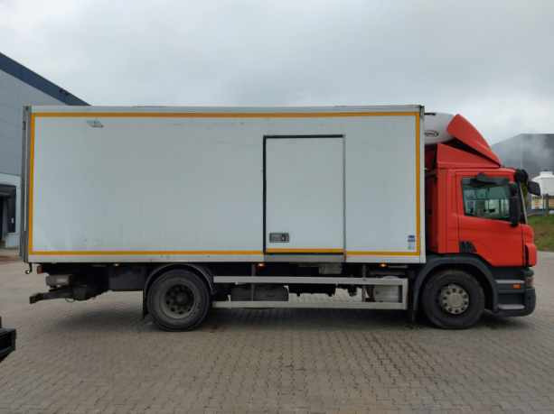 Czerwona ciężarówka z białą naczepą chłodniczą, zaparkowana na brukowanej powierzchni, widok z boku.