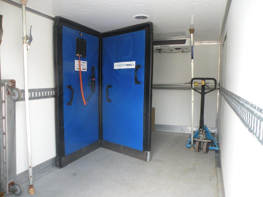 Wnętrze chłodni samochodowej z otwartymi niebieskimi drzwiami izolacyjnymi, widoczny agregat chłodniczy i wózek paletowy.