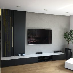 EMKA Marczak Łukasz - Nowoczesna ściana telewizyjna z podświetlanymi panelami pionowymi, szafkami RTV w kolorze czarno-białym i dekoracyjnym tynkiem na ścianie w salonie.