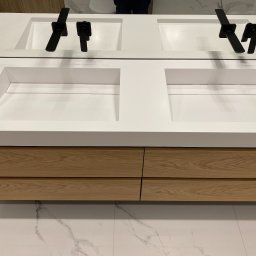 EMKA Marczak Łukasz - Nowoczesna łazienka z podwójną, wpuszczaną umywalką z białego konglomeratu, czarną armaturą i szafką z jasnego drewna na tle marmurowej podłogi.