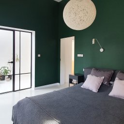 Maria Green Design - Nowoczesna sypialnia z ciemnozielonymi ścianami, białymi podłogami i dużym, okrągłym abażurem z włókna, minimalistyczna lampka ścienna i widok na patio przez przeszklone drzwi.