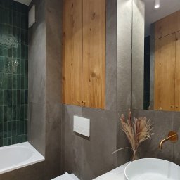 Maria Green Design - Nowoczesna łazienka z zielonymi płytkami w strefie prysznica, szarymi płytkami na ścianach, drewnianymi szafkami wiszącymi i pod umywalką, białą ceramiką i złotą armaturą.