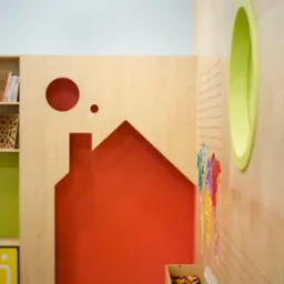Pokój dziecięcy z drewnianymi elementami w kształcie domu, koła i owalu, pomalowany na czerwono, zielono i żółto, z półkami na książki i pojemnikami na zabawki.