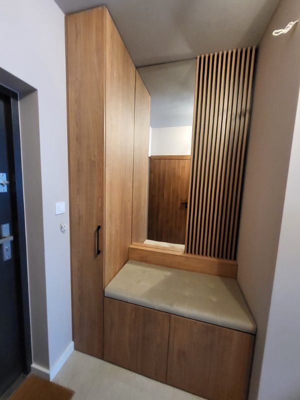 Drewniana zabudowa przedpokoju z szafą, siedziskiem z tapicerowanym obiciem i lustrem z dekoracyjnymi lamelami.