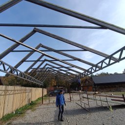 Dom-bud Serhii Varetskji - Metalowa konstrukcja dachu w trakcie budowy, widok z dołu na niebo. Na pierwszym planie osoba w niebieskiej kurtce, w tle drewniany budynek.