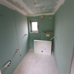 Dom-bud Serhii Varetskji - Wnętrze łazienki w trakcie wykańczania: ściany z płyt gipsowo-kartonowych, widoczne instalacje wodne, przygotowane miejsce na brodzik. Surowe, jasne światło.