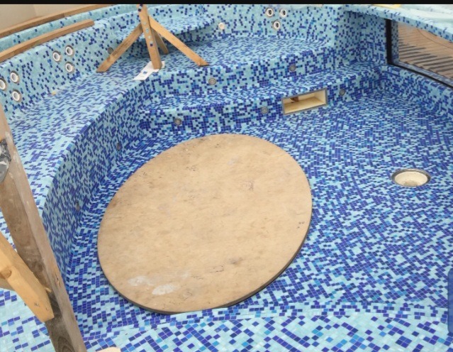 Niebieska mozaika w basenie jacuzzi w trakcie wykańczania, widoczne podpory drewniane i okrągła pokrywa.