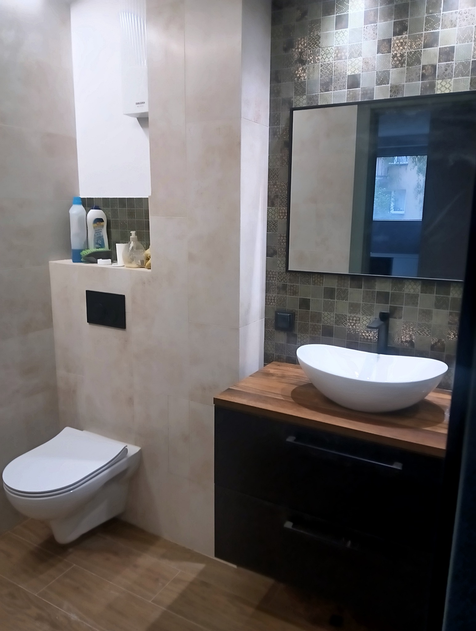 Nowoczesna łazienka z wiszącą toaletą, umywalką nablatową na drewnianym blacie i mozaiką na ścianie.