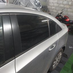 Salon auto wrappingu - Srebrny samochód z przyciemnionymi szybami tylnymi, zaparkowany w warsztacie z widocznym motocyklem w tle.