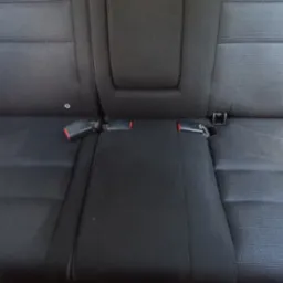 Czarne, teksturowane tylne siedzenie samochodowe z widocznymi zapięciami pasów bezpieczeństwa, sfotografowane w jasnym świetle dziennym.