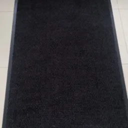 Ciemnoszary, prostokątny wycieraczka na beżowej podłodze z płytek, widok z góry.