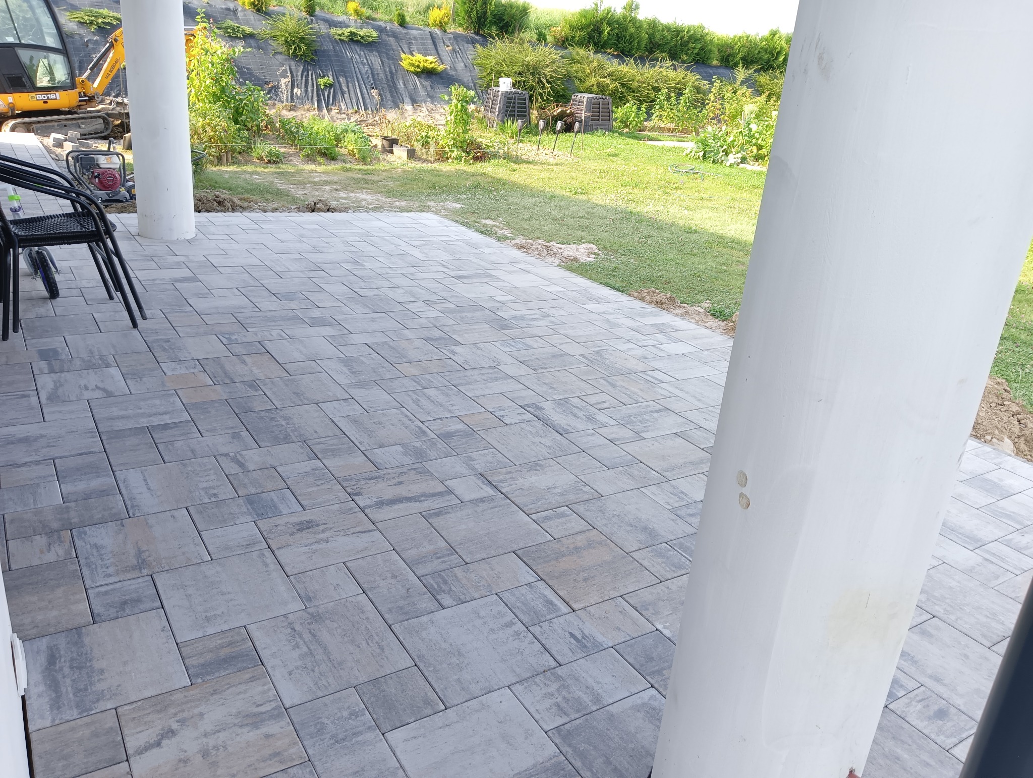 Nowo ułożona, szara kostka brukowa na tarasie z widocznym minikoparką i zagospodarowanym terenem zielonym w tle.