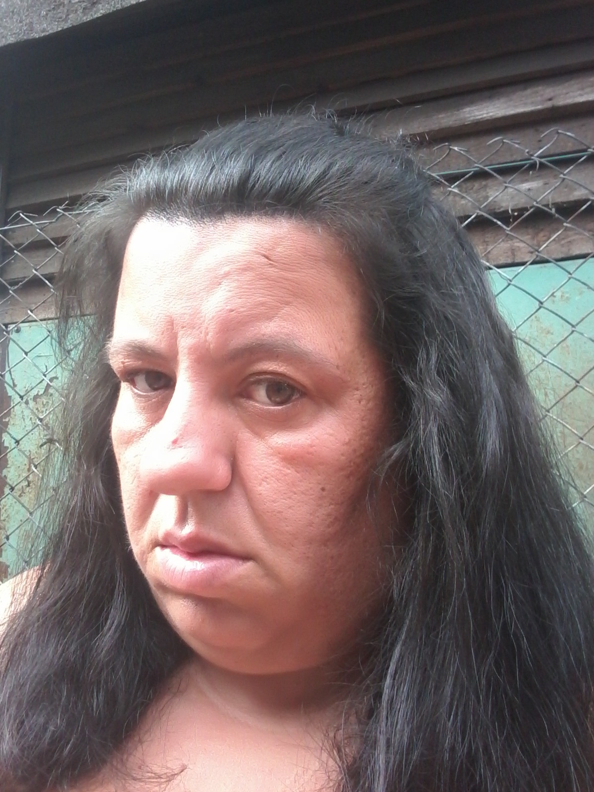 Portret kobiety z ciemnymi włosami na tle drewnianej ściany i siatki.