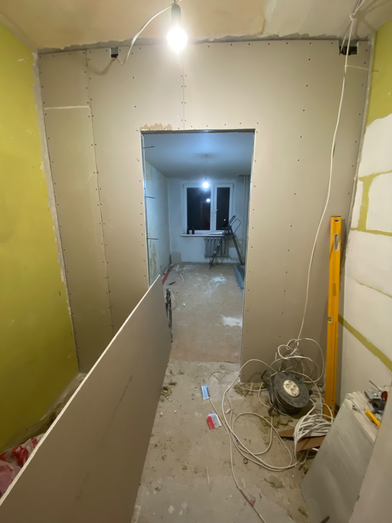 Wnętrze w trakcie montażu płyt kartonowo-gipsowych, widoczna konstrukcja ścian działowych, surowy stan wykończenia, przewody elektryczne i poziomica.