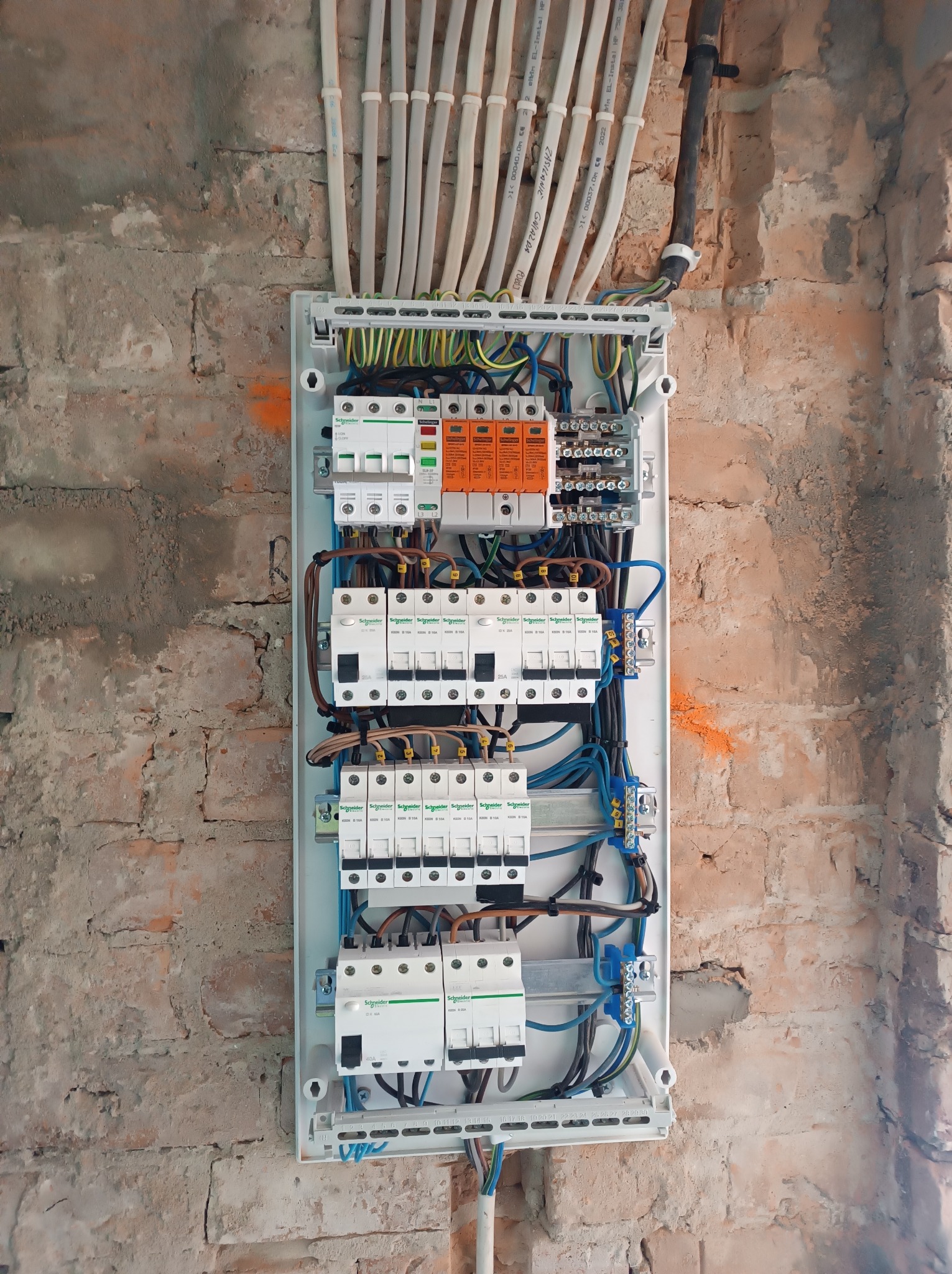 Otwarta skrzynka elektryczna z zainstalowanymi bezpiecznikami i przewodami na tle surowej ściany z cegły.